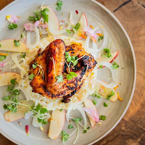 The image shows a plate with grilled chicken on a bed of rice, garnished with sliced apples, onions, and fresh green herbs.