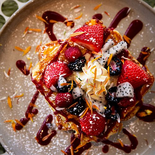 A delectable dessert topped with strawberries, dragon fruit, and various berries, drizzled with syrup and garnished with powdered sugar and coconut flakes.