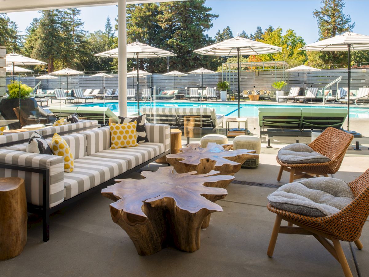 The image shows a stylish outdoor seating area with a pool in the background, featuring modern furniture and large poolside umbrellas, ending the sentence.