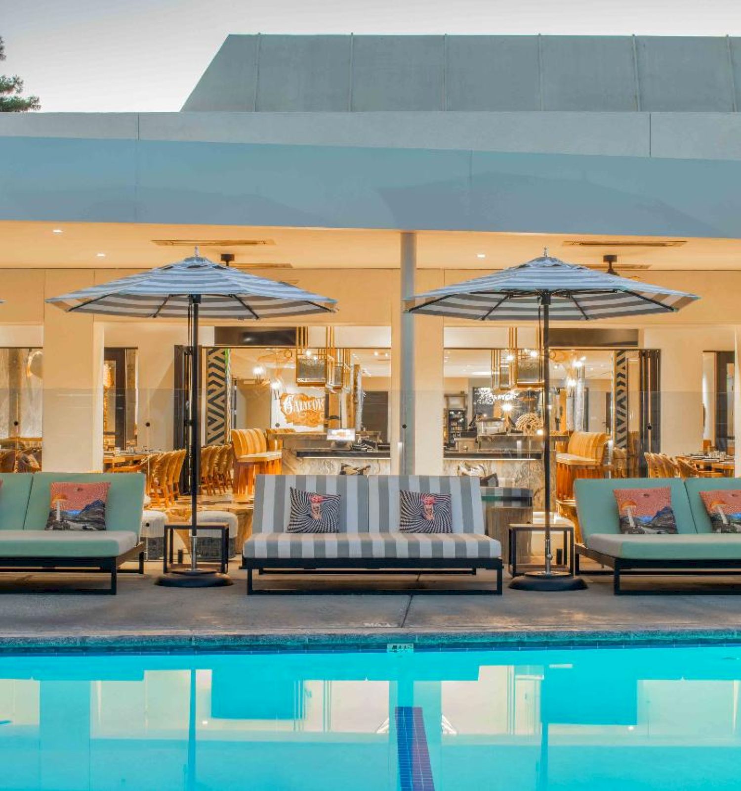 The image features an outdoor pool area with lounge chairs and umbrellas, set in front of a modern building with large windows.